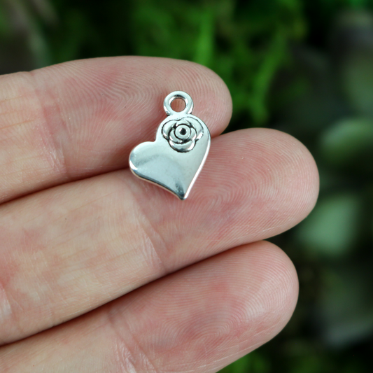 silver tone heart shaped charm with a rose detail in the upper right side