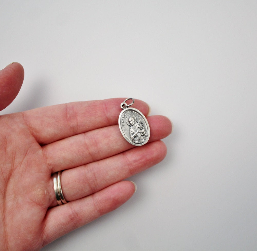 womans hand holding catholic patron saint maria goretti medal