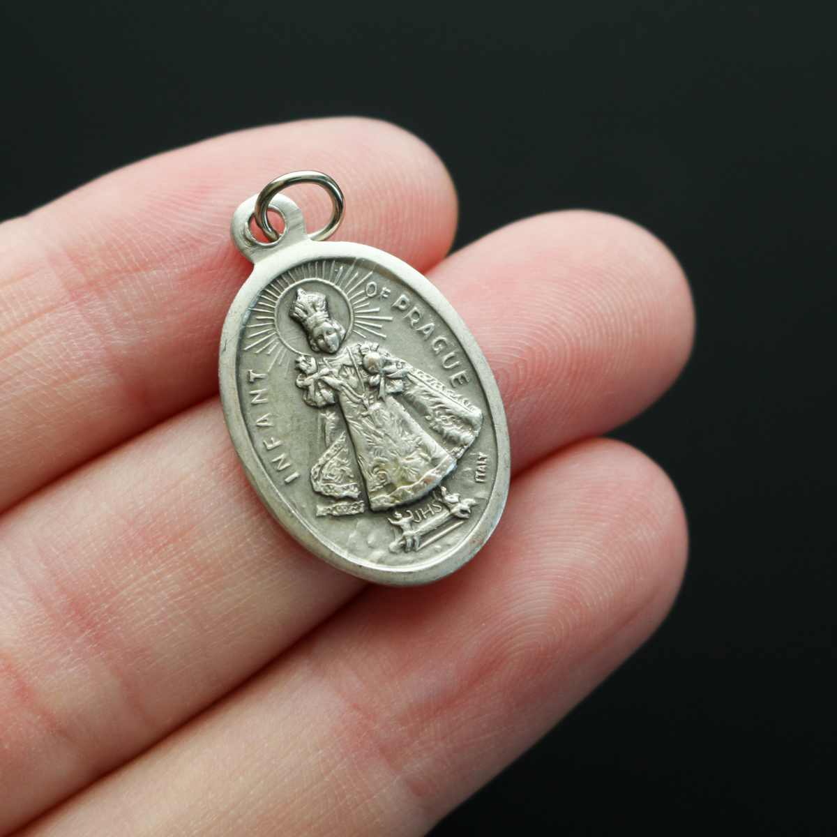 Infant Jesus of Prague medal that depicts the Infant Jesus on the front and is marked "Pray For Us" on the back