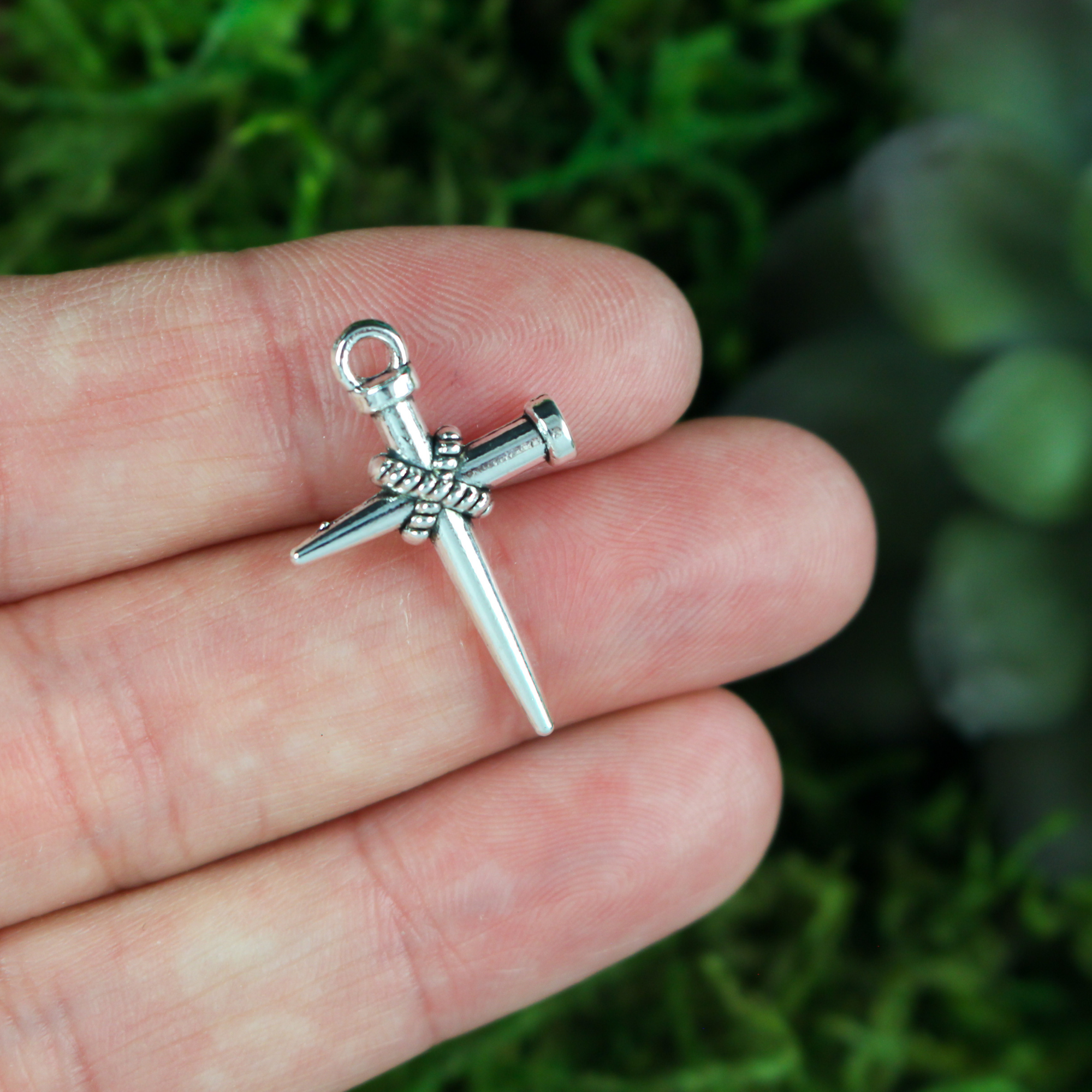 Silver-tone cross charm of two nails bound together to symbolize peace and reconciliation