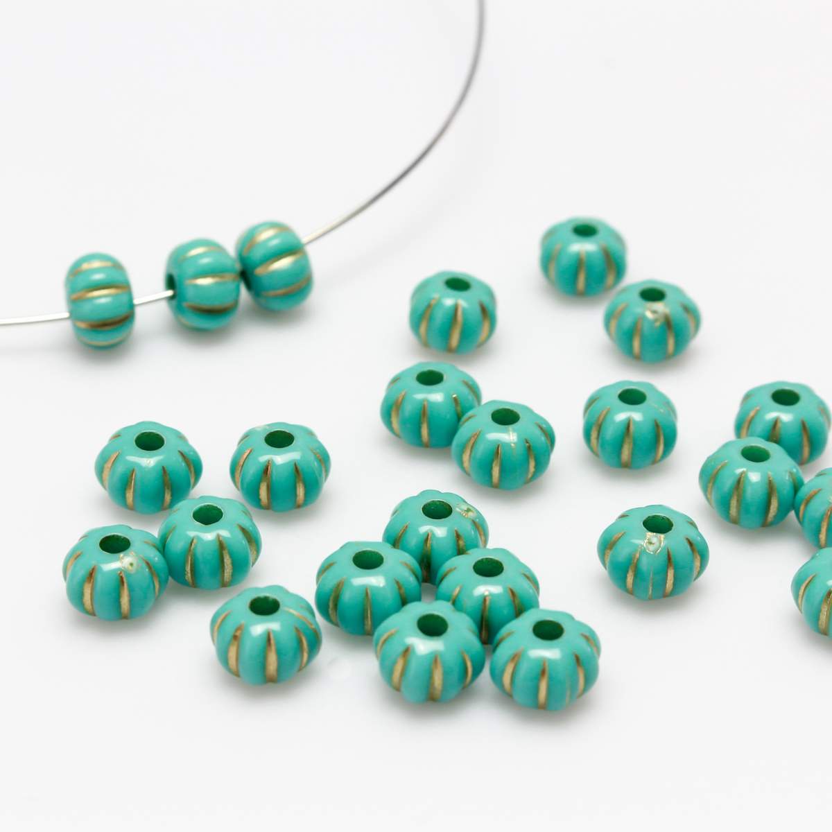 Acrylic pumpkin shaped beads that are turquoise in color with a gold metal detailing along the indents.