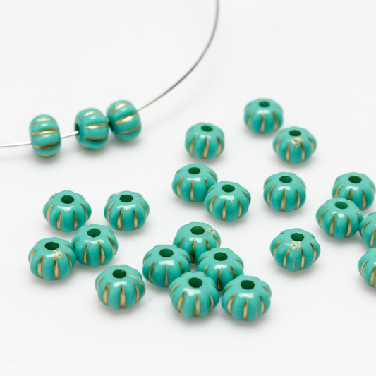 Acrylic pumpkin shaped beads that are turquoise in color with a gold metal detailing along the indents.