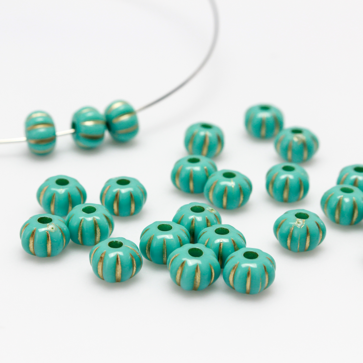 Acrylic pumpkin shaped beads that are turquoise in color with a gold metal detailing along the indents.