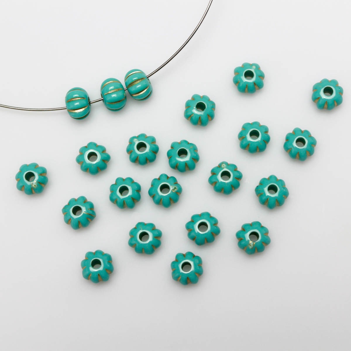 Acrylic pumpkin shaped beads that are turquoise in color with a gold metal detailing along the indents.