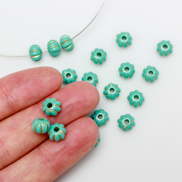 Acrylic pumpkin shaped beads that are turquoise in color with a gold metal detailing along the indents.
