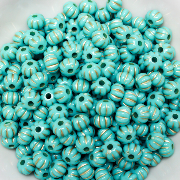 Acrylic pumpkin shaped beads that are turquoise in color with a gold metal detailing along the indents.