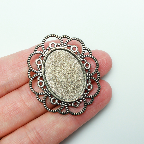 Silver tone oval bezel brooch pin with an ornate filigree border. The tray size on this bezel is 25mm x 18mm