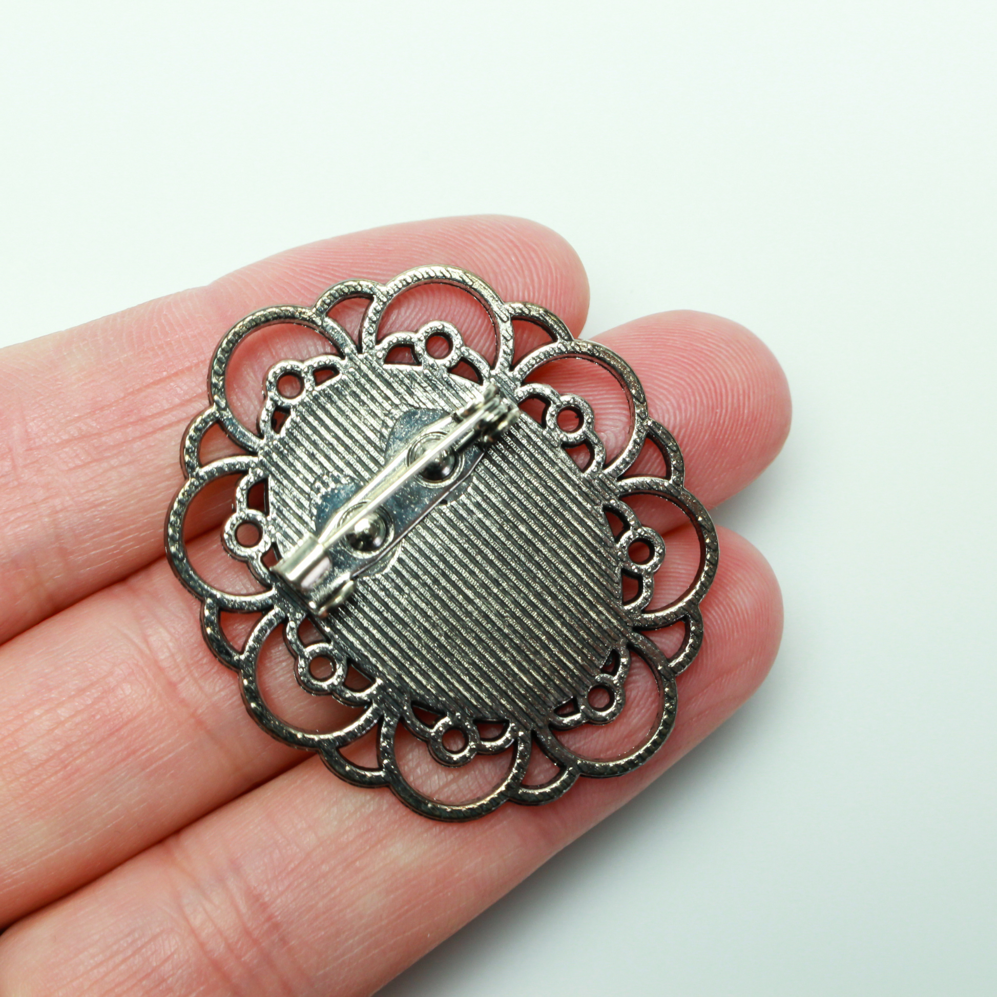 Silver tone oval bezel brooch pin with an ornate filigree border. The tray size on this bezel is 25mm x 18mm