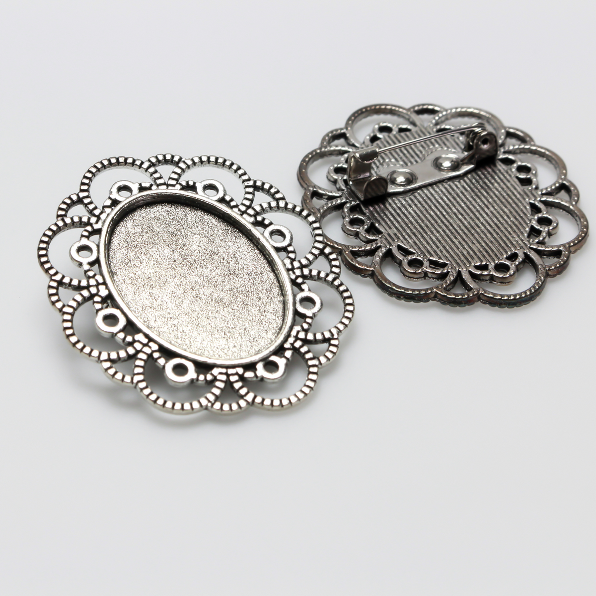 Silver tone oval bezel brooch pin with an ornate filigree border. The tray size on this bezel is 25mm x 18mm