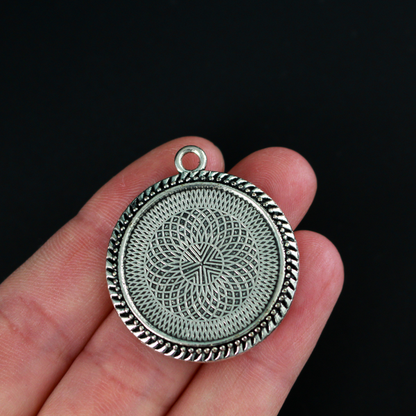 Round pendant cabochon setting in an antiqued silver color. There is a pattern along the edge of the cup. The tray fits 25mm cabochons