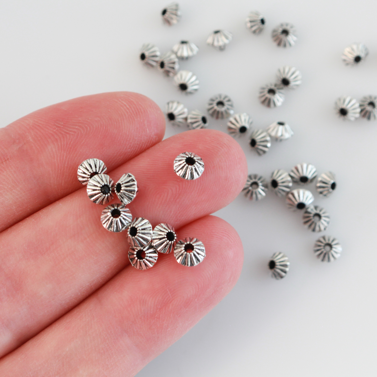 100 metal bicone shaped spacer beads with an antiqued silver finish and a corrugated pattern