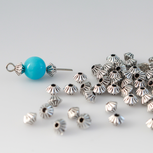 100 metal bicone shaped spacer beads with an antiqued silver finish and a corrugated pattern