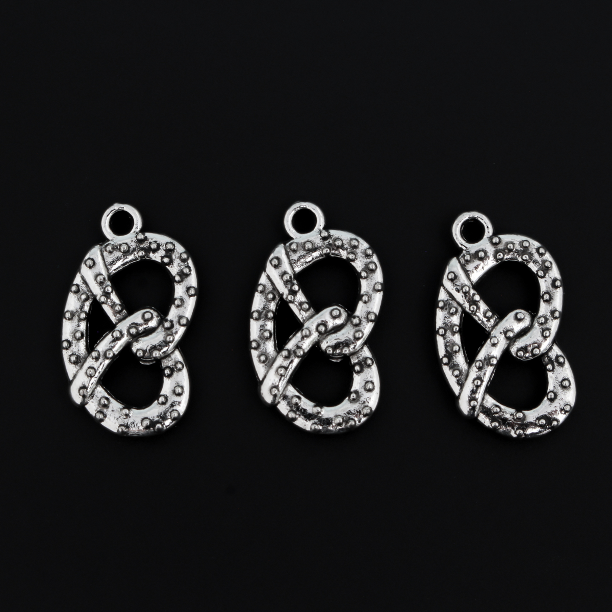 Small silver tone pretzel charm, sold in sets of three. This is a double-sided charm and looks the same on both sides.