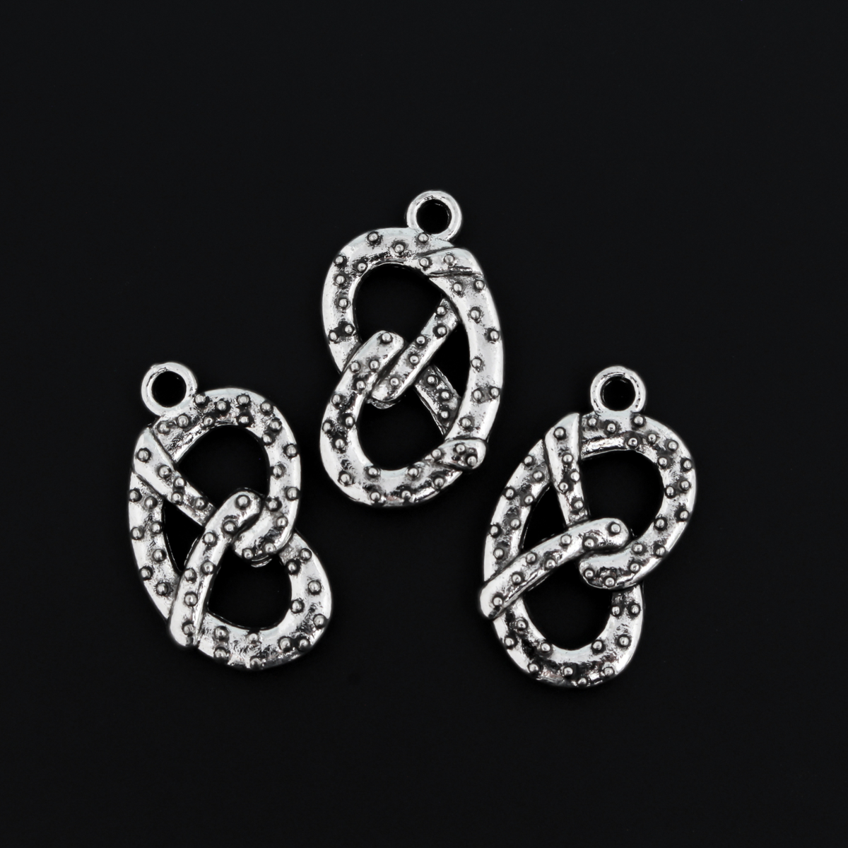 Small silver tone pretzel charm, sold in sets of three. This is a double-sided charm and looks the same on both sides.