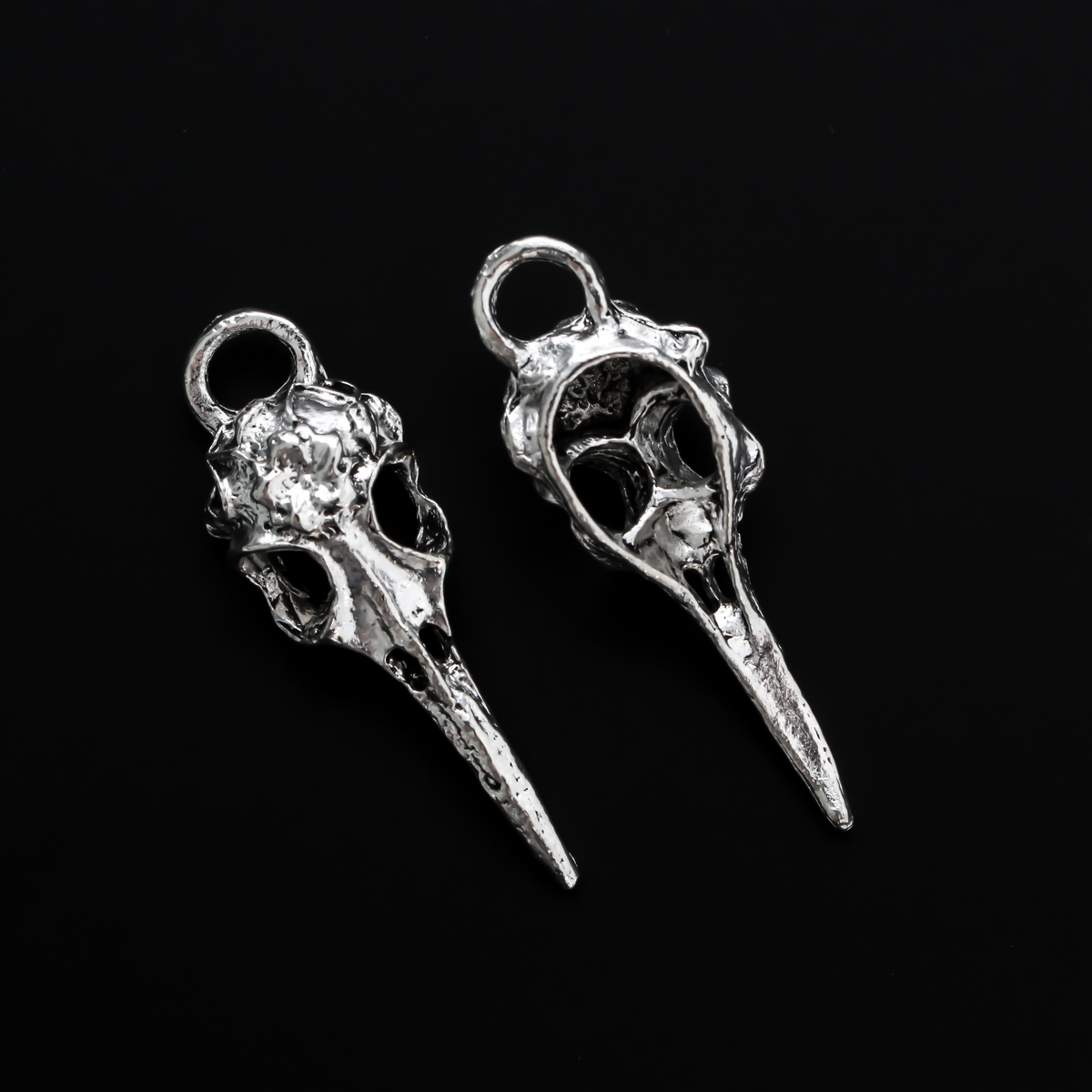 Antiqued silver tone raven skull charms that have a flower design on the top