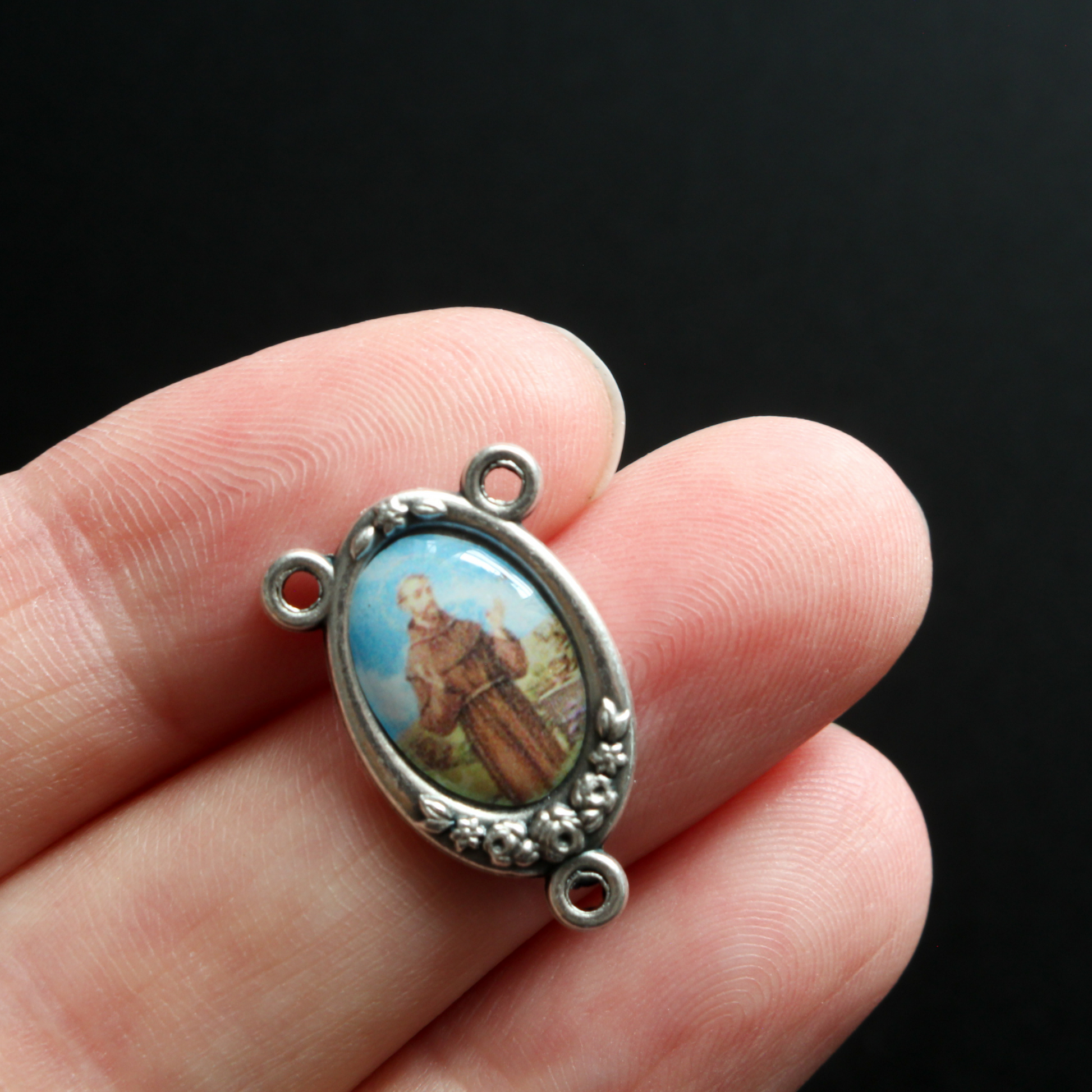 rosary center that has a full-color image of Saint Francis of Assisi inlaid in a silver oxidized center with flower details on the edge