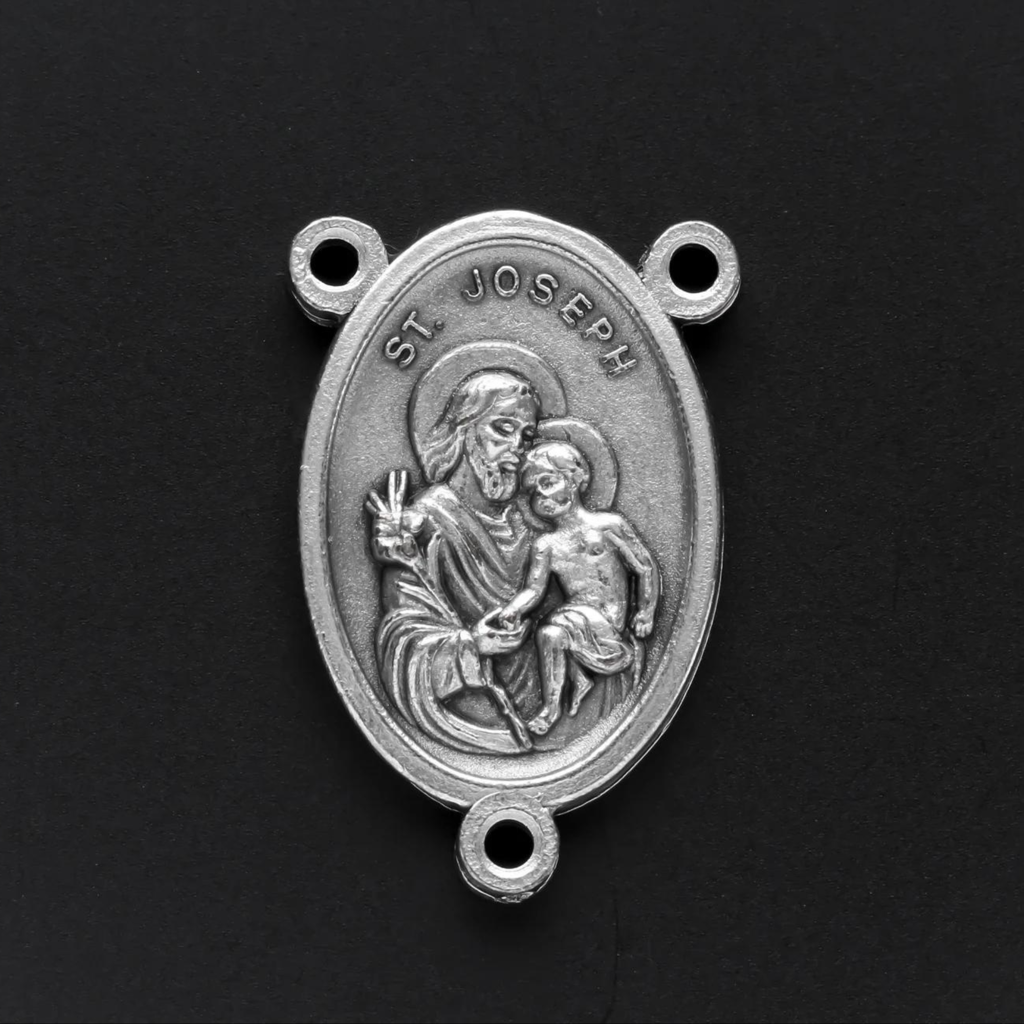 Saint Joseph rosary centerpiece. The front of the medal depicts Saint Joseph holding child Jesus in one arm and a lily in the other. The reverse side is marked "Pray For Us"