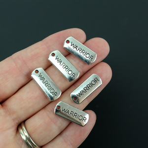 the word warrior engraved on a small silver rectangle charm